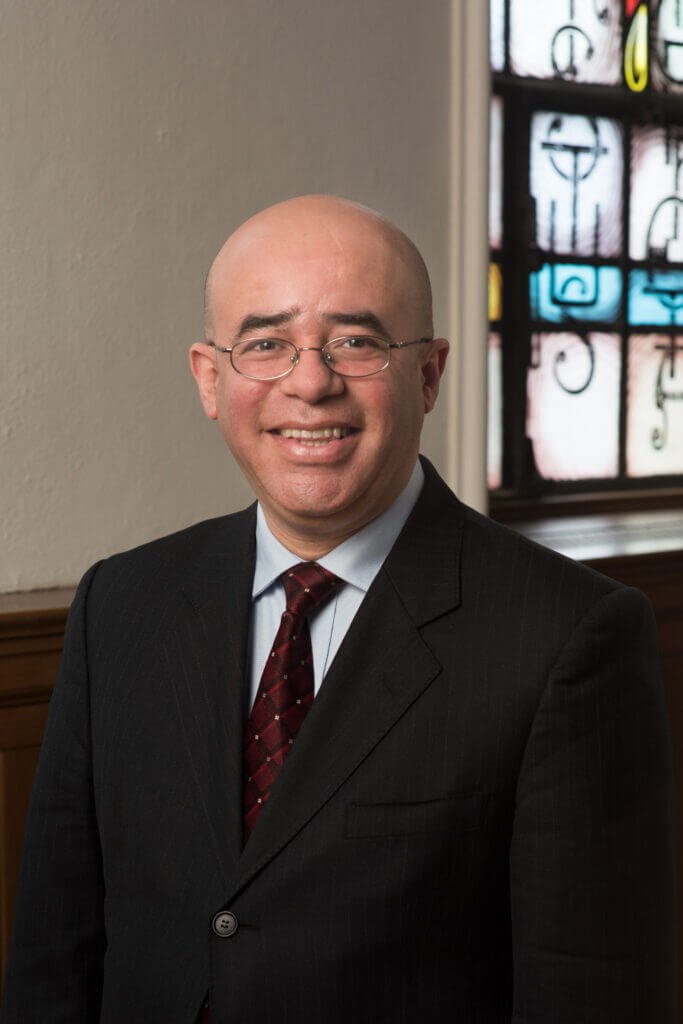 A man in pink is wearing glasses and a necklace